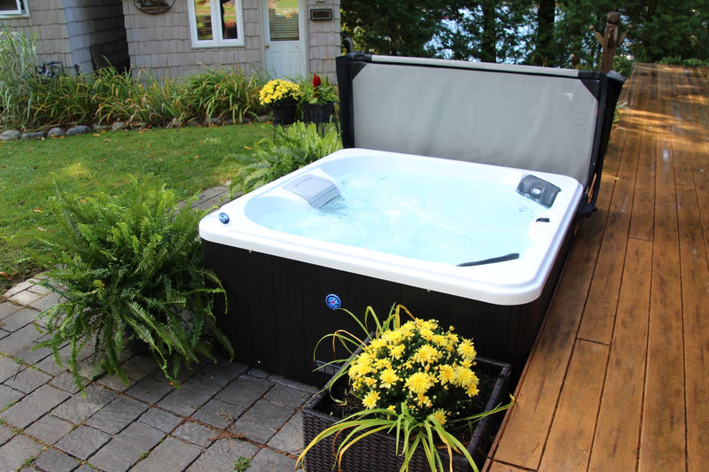 Hard-shell hot tub with clear bubbling water and the cover folded back on a patio beside autumn chrysanthemums