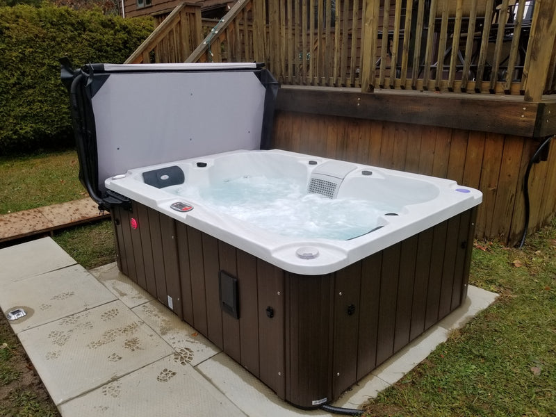 Hard-shell hot tub with the jets running and the cover folded back, on a paved base in an autumn garden