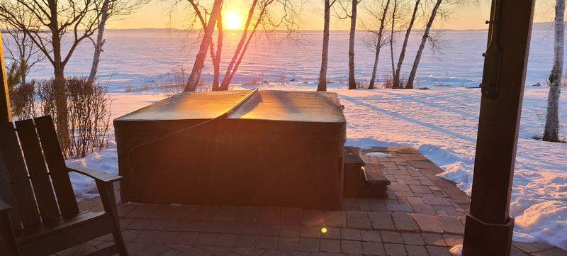 Hot tub with its cover closed on a paved patio at winter sunset, beside a frozen lake