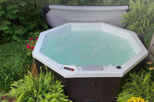 
Octagonal hot tub on a garden deck with the cover open and clear water, surrounded by ferns and flowers