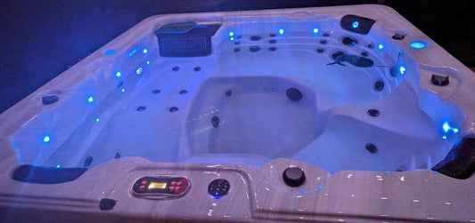 
Hard-shell hot tub lit with blue LEDs at night, with a small floating thermometer in the water