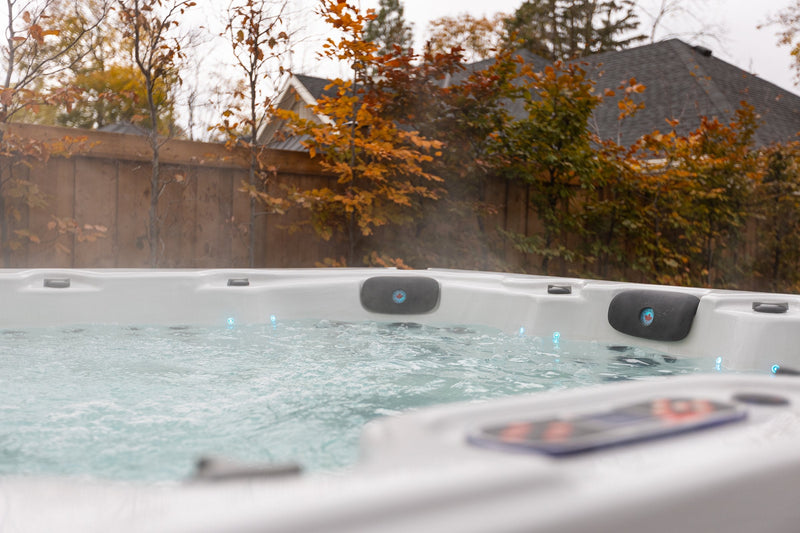 Steam rising from a hard-shell hot tub with its control panel in the foreground and autumn trees behind