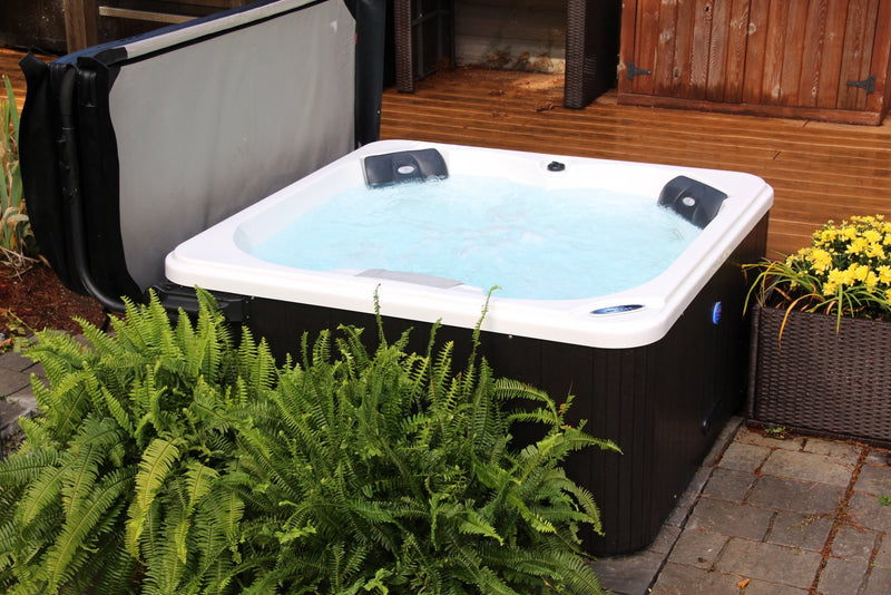 Open hard-shell hot tub with clear water beside ferns and yellow autumn chrysanthemums on a patio