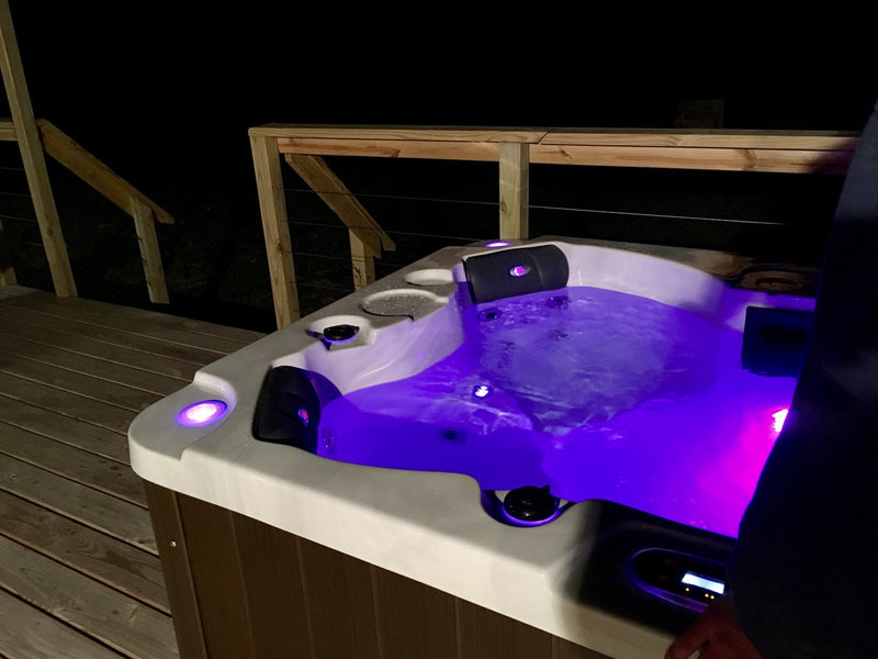 Hard-shell hot tub on a timber deck at night with purple LED lights and the topside control panel display lit