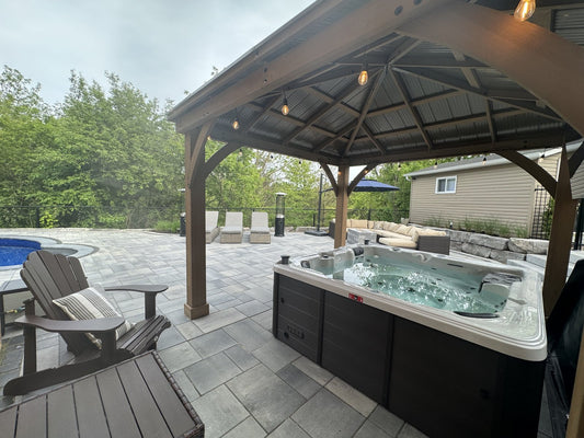 
Hard-shell hot tub with the cover off under a timber gazebo on a stone patio, with rows of jets in the seats