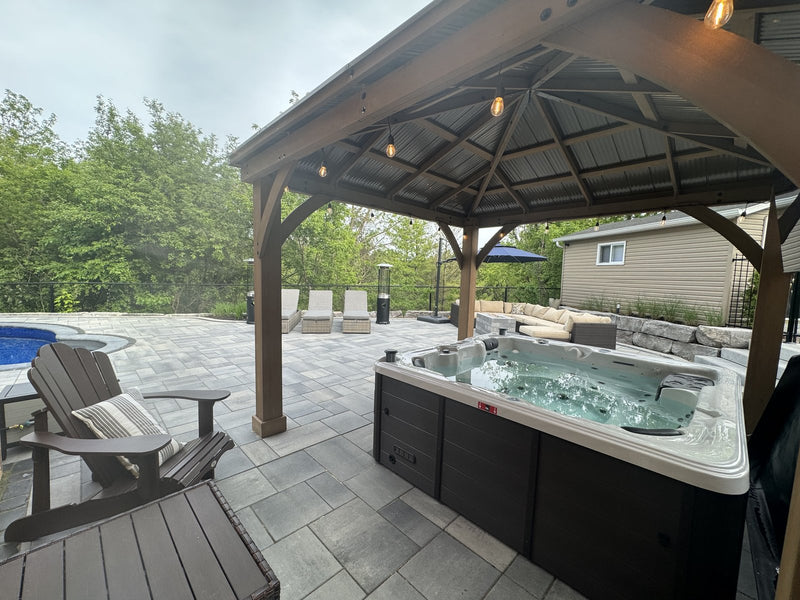 Hard-shell hot tub with the cover off under a timber gazebo on a stone patio, with rows of jets in the seats