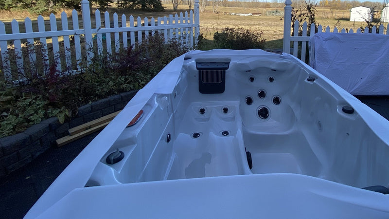 New acrylic hot tub sitting empty on a garden base with its protective film still on and the wrapped cover beside it, on a clear autumn day
