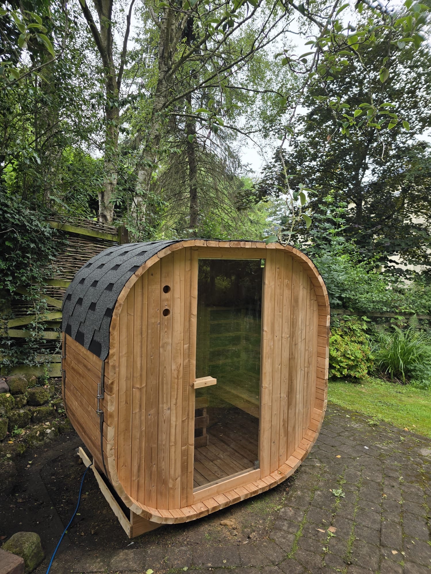 Outdoor Oval Barrel sauna sited on a slate patio, owner's cherry-blossom trim around the doorway for a garden party
